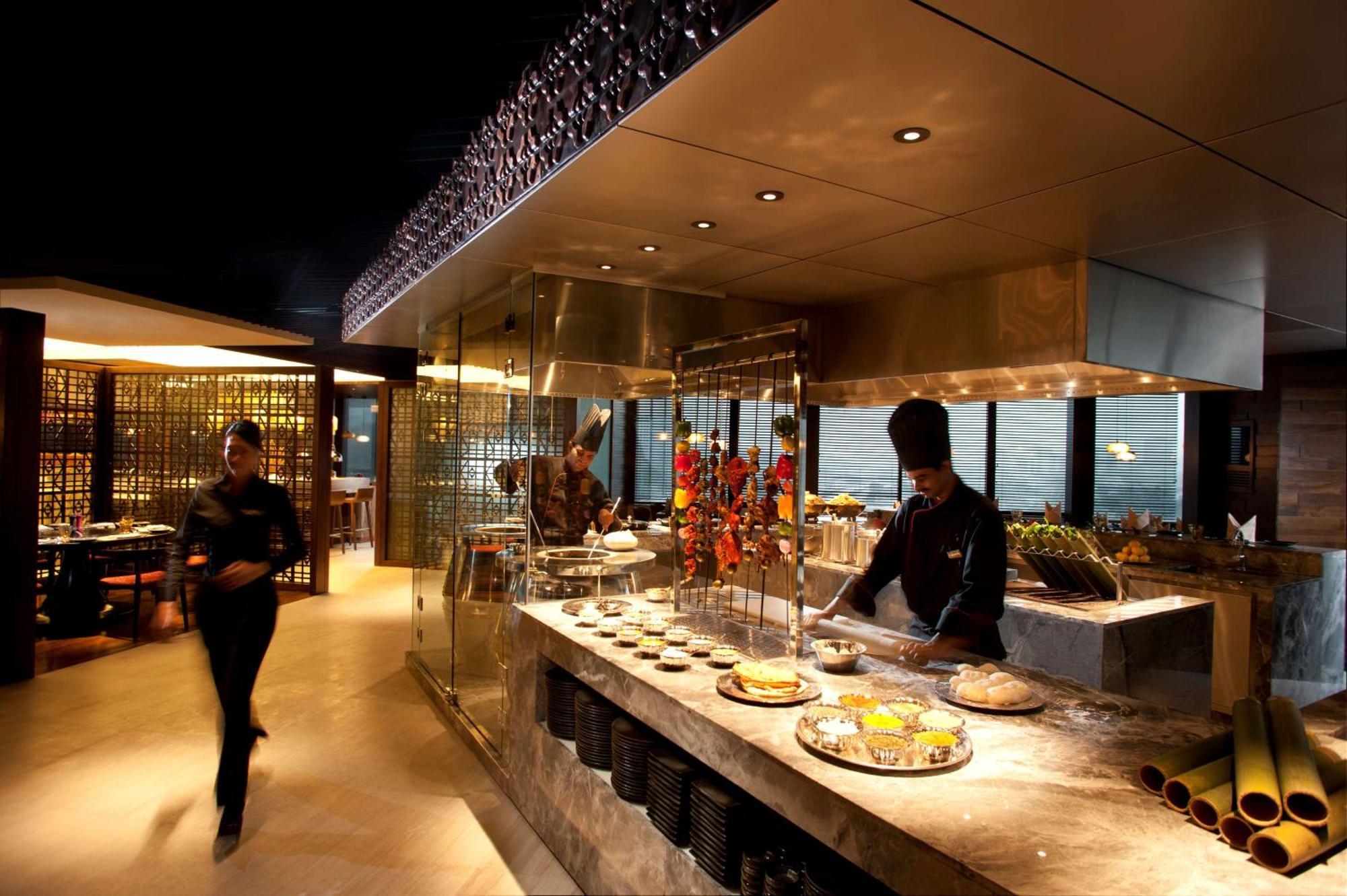 Готель Doubletree By Hilton Куала-Лумпур Екстер'єр фото The photo depicts a modern restaurant interior with a sleek and sophisticated design. In the foreground, there is a chef working at an open kitchen area, preparing food. The kitchen features a glass display that showcases a variety of dishes, along w