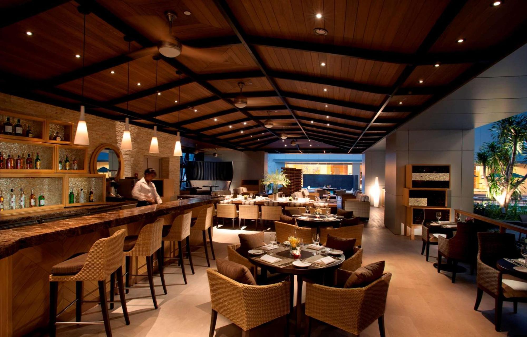 Готель Doubletree By Hilton Куала-Лумпур Екстер'єр фото The photo shows an upscale restaurant interior with a warm and inviting ambiance. There is a large wooden bar area on one side, with bar stools arranged around it. The ceiling features wooden beams and modern lighting fixtures, creating a cozy atmosp
