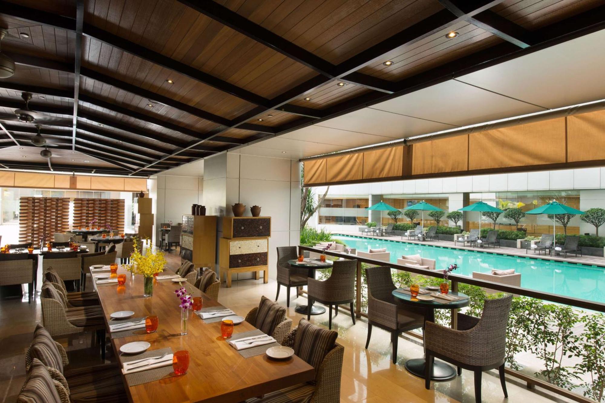 Готель Doubletree By Hilton Куала-Лумпур Екстер'єр фото The photo shows an indoor restaurant area with a modern and stylish design. There are several tables set for dining, featuring place settings and drinks. Large windows allow for a view of a swimming pool outside, which is adorned with umbrellas. The 