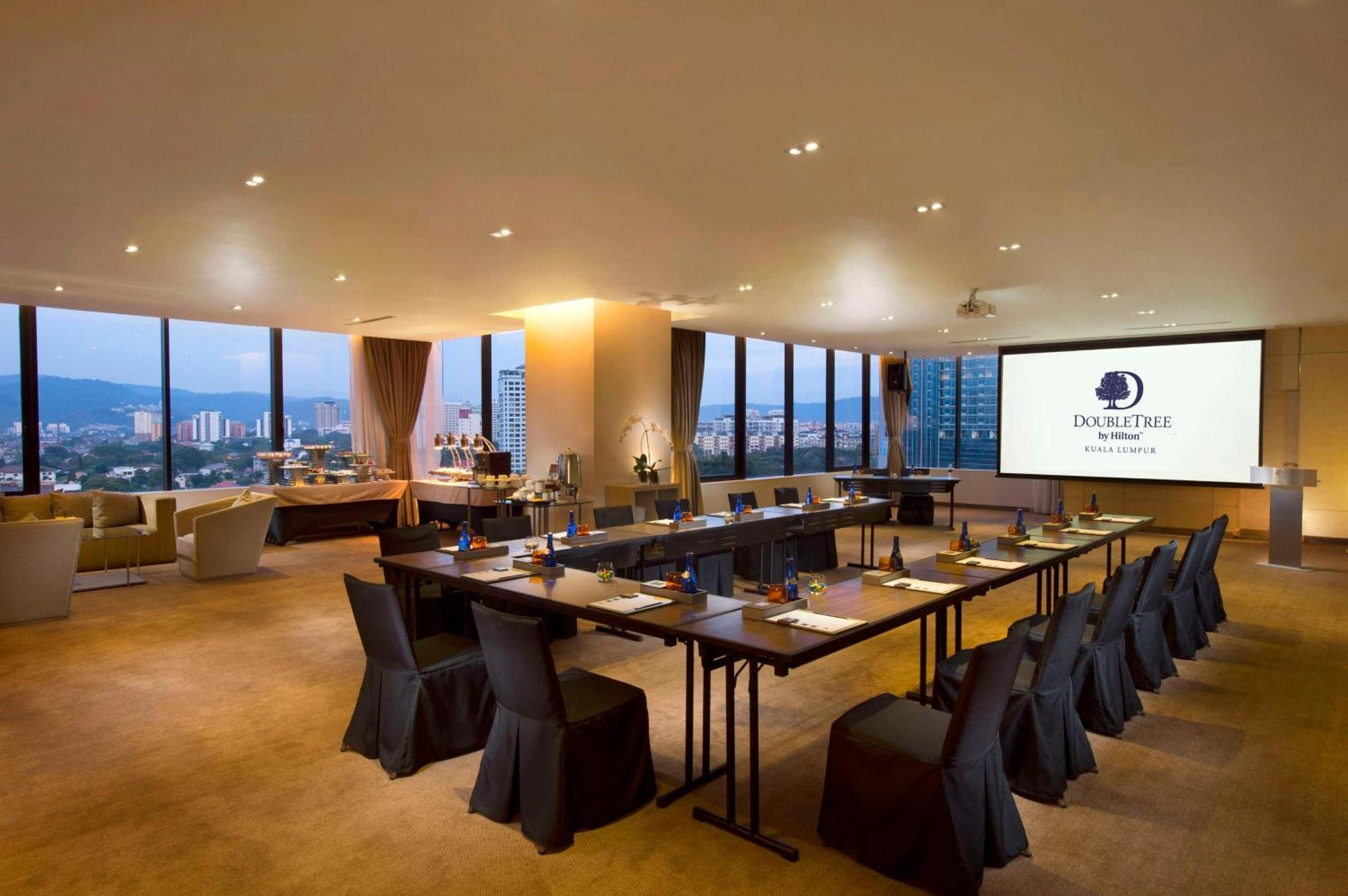 Готель Doubletree By Hilton Куала-Лумпур Екстер'єр фото The photo shows a modern conference room. It features a long table arranged for a meeting, with black chairs and notepads placed at each seat. The room has large windows that let in natural light and offer a view of the city outside. On one wall, the