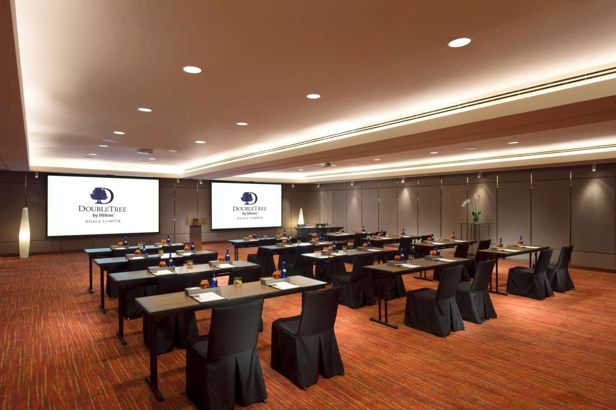 Готель Doubletree By Hilton Куала-Лумпур Екстер'єр фото The image shows a conference or meeting room setup. There are several rows of tables arranged for participants, each covered with a black tablecloth. The tables are equipped with stationery, suggesting that the space is intended for a professional ga
